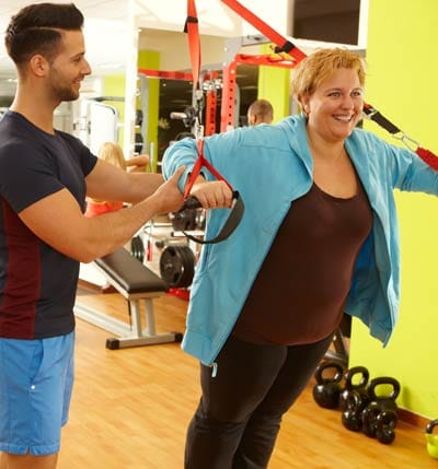 American fitness coach training obese person exercising indoors gym